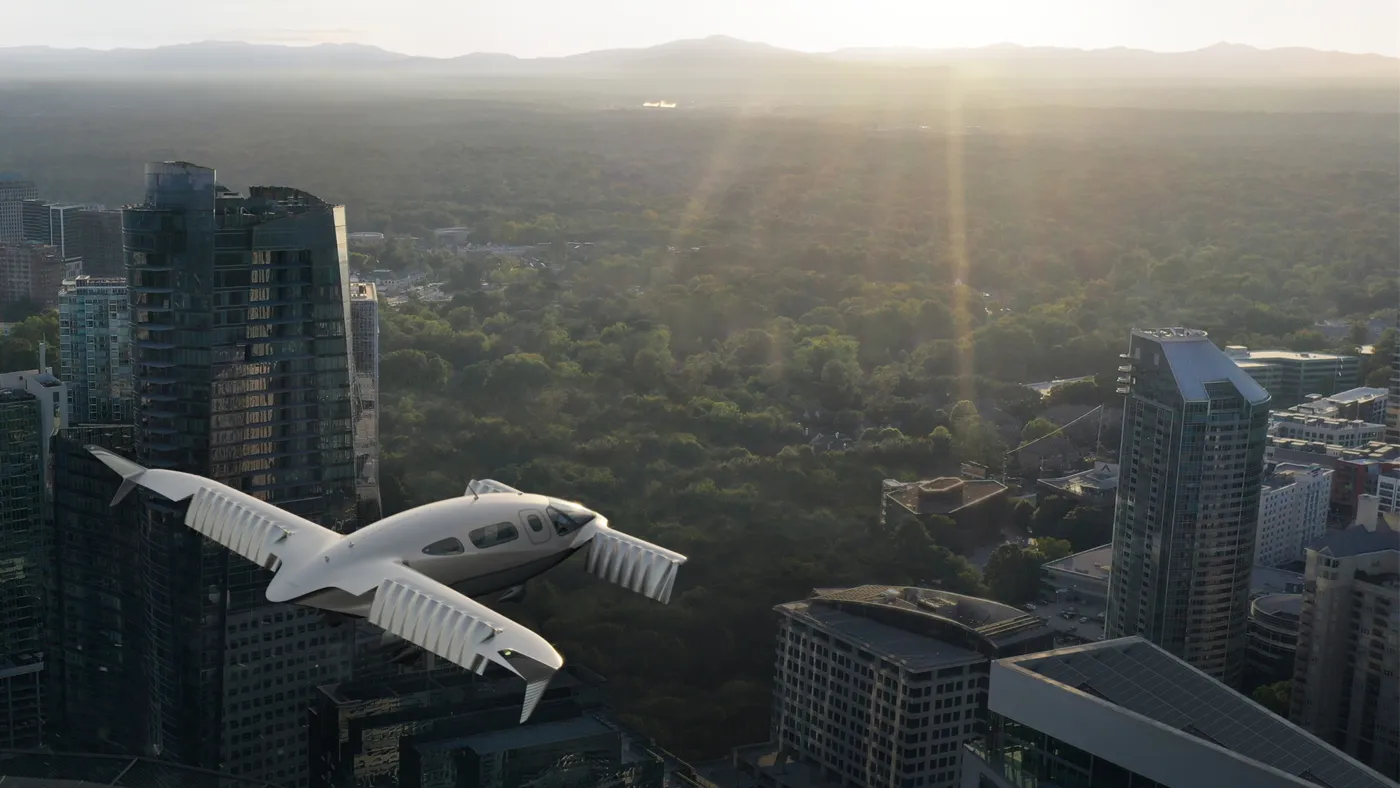 Flugmaschine fliegt über eine Stadt mit angrenzenden Wald hinweg