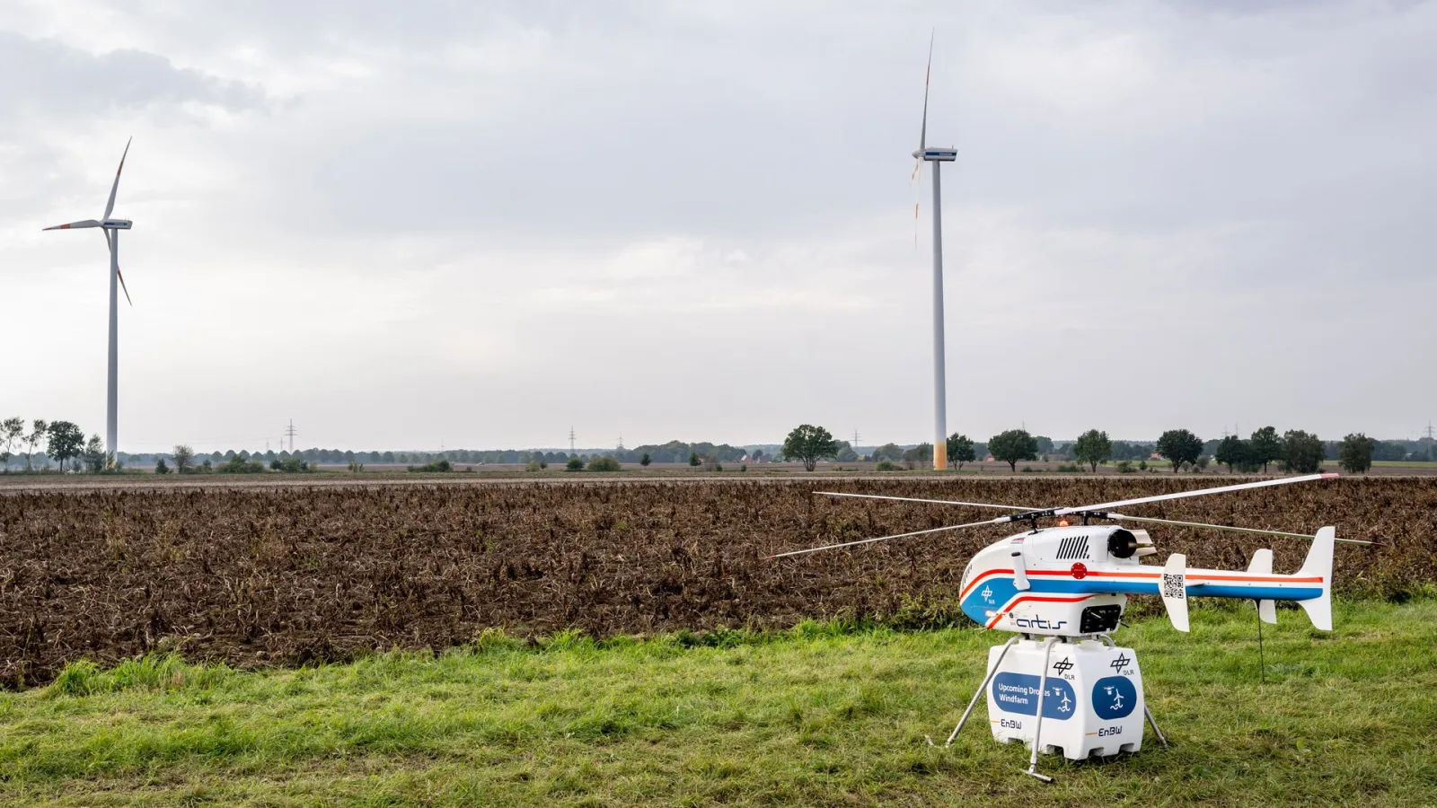 DLR-Hubschrauber superARTIS evor Windrädern. Die Flugversuche fanden im Rahmen des Projekts „Upcoming Drones Windfarm“ statt. 